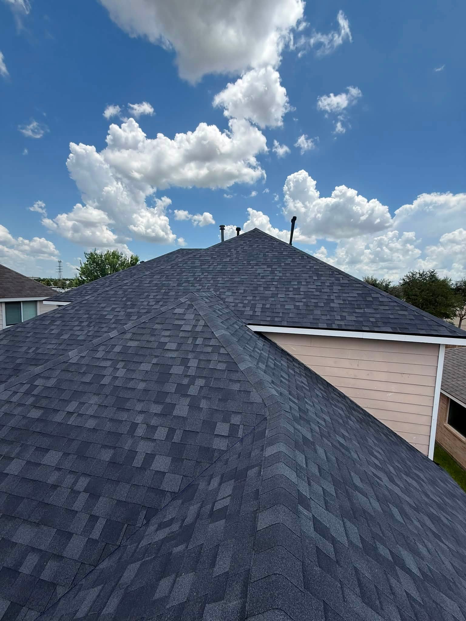 Aerial view of a finished charcoal architectural shingle roof under blue Houston sky